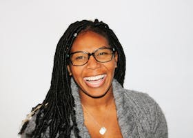 A vibrant portrait of a smiling woman with dreadlocks and glasses, exuding joy.